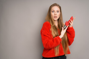 A white-skinned girl with long hair in a red jacket looks surprised holding a vibrator or a dildo...