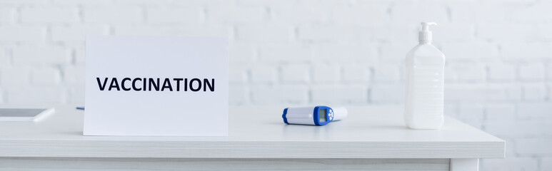 sign plate with vaccination lettering near pyrometer and dispenser bottle with hand sanitizer, banner