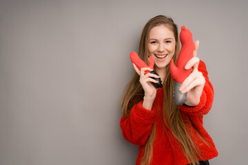 An attractive girl of European appearance in a red sweater happily holds a red phallus