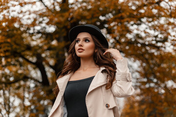 Autumn portrait of beautiful glamorous young woman with curly hair with vintage hat in gray fashionable coat walking outdoors with colorful fall foliage