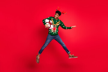 Fototapeta na wymiar Full length body size view of trendy handsome cheerful guy jumping holding gift having fun isolated over vivid red color background