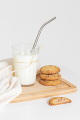 Homemade cookies on wooden cutting board and a glass of milk on white background.