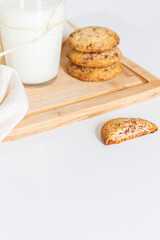 Homemade cookies on wooden cutting board and a glass of milk on white background.