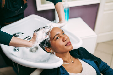 Professional hairdresser washing hair of a middle aged African American woman in hair salon.
