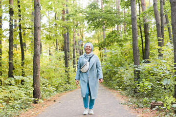 Islamic young woman wearing hijab standing on autumn park background. Modern arabian muslim girl.