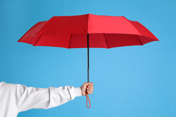 Woman with open red umbrella on light blue background, closeup