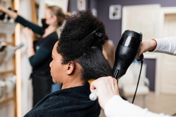 An middle aged African American woman on a curly hair straightening treatment at a hair salon. - obrazy, fototapety, plakaty