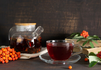 Tea with mint, currant, mountain ash and mint in a transparent cup on a dark wooden table. A teapot with tea leaves on a light napkin in the background