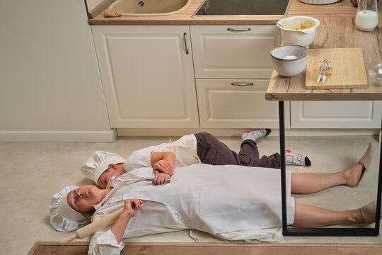 Funny Mom And Son Relax In The Kitchen After Cooking. A Tired Woman And A Boy Are Lying On The Kitchen Floor