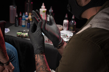Latin person tattooing arm, with adequate security measures in his workplace happy and calm...