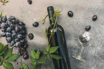 Bottle of red wine, green vine, wineglass and ripe grape on vintage dark stone table background....