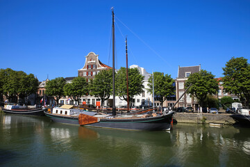 Fototapeta na wymiar Dordrecht, Netherlands - July 9. 2021: View on typical inland water canal harbor with old sail ship against blue summer sky