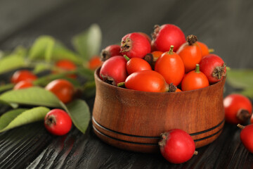 Ripe rose hip berries with green leaves on black wooden table, closeup