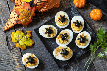 Halloween funny idea for party food. Halloween creative set stuffed eggs with paprica and bat on a wooden table.