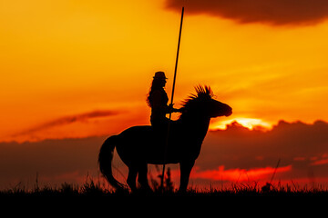 dark silhouette of a woman on horseback against the sunset with a long spear