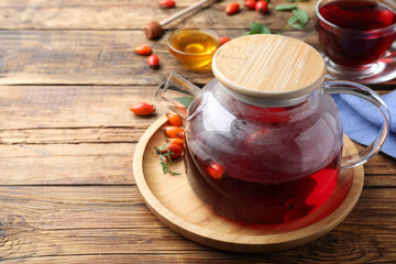Teapot with aromatic rose hip tea and fresh berries on wooden table, space for text