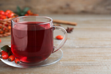 Aromatic rose hip tea and fresh berries on wooden table, space for text