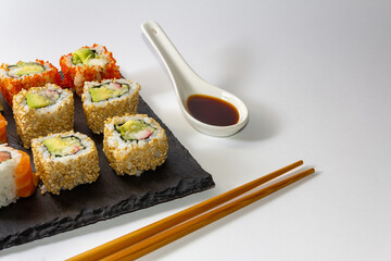 Gourmet sushi tray on slate surface on white background with soy sauce and chopsticks. Copy space. Selective focus.