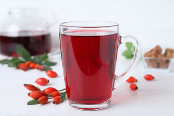 Aromatic rose hip tea and fresh berries on white wooden table, closeup