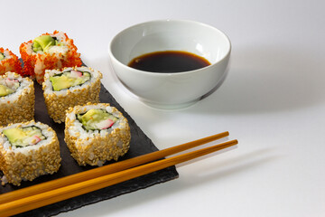 Gourmet sushi tray on slate surface on white background with soy sauce and chopsticks. Copy space. Selective focus.