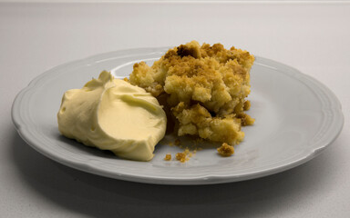 Sweet desserts. Apple crumble slice of cake with cream on a white dish in the kitchen table.	