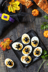 Obraz na płótnie Canvas Halloween funny idea for party food. Halloween creative set stuffed eggs with paprica and bat on a wooden table. Top view flat lay background. 
