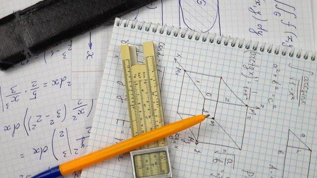Vintage slide rule for performing of the mathematical computations, leather slide rule case and ballpoint pen lie on the pieces of paper with mathematical calculations 