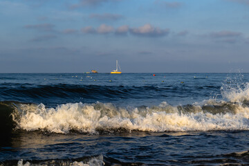 A seascape overlooking a sea foam wave that rolls ashore and a lonely boat far on the horizon.