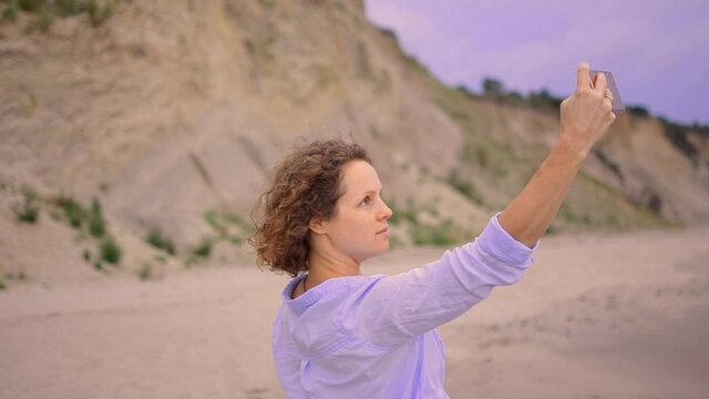 Close up of cheerful woman in blue dress taking a selfie at the Baltic beach.