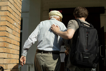 The grandson helps grandpa walk to the entrance to the hospital. A volunteer leads a pensioner to...