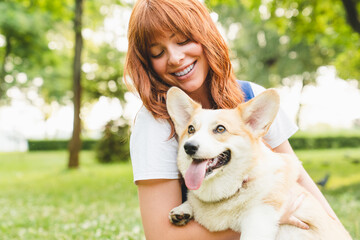 Spending free time with pet together. Happy young caucasian young woman teenage girl walking having fun taking care of her pet dog welsh corgi outdoors in park, forest, garden.