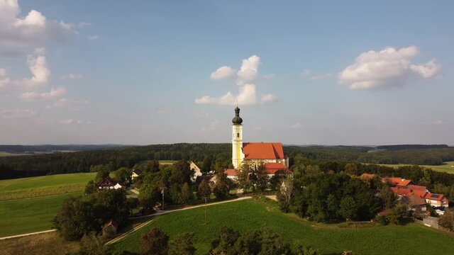 Drone circling around the village Eichlberg near Hemau with church of pilgrimage and surrounding rural area on top of a hill in Bavaria in sunlight