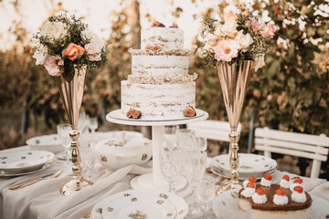 Closeup of a white wedding cake with small bouquets of flowers in golden vases.