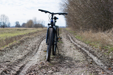 Fototapeta na wymiar Mountain bike. stands on a field road. spring or autumn. concept of cycling, repair or breakage. sports, outdoor activities. bad weather, mud, road washed out after rain. trail, front wheel in focus.
