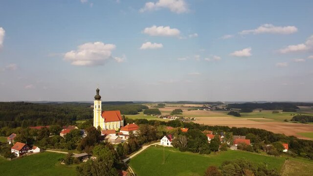 Drone circling around the village Eichlberg near Hemau with church of pilgrimage and surrounding rural area on top of a hill in Bavaria in sunlight