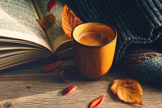  Autumn drink, A mug of hot coffee on a wooden table with a book, warm sweater with yellow autumn leaves vintage tone. Still life seasonal relax concept.