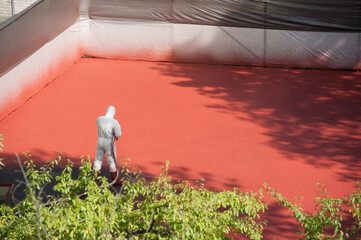 Obraz premium Liquid rubber coating process. A worker dressing security suit spraying the rubber on the surface using a spray gun