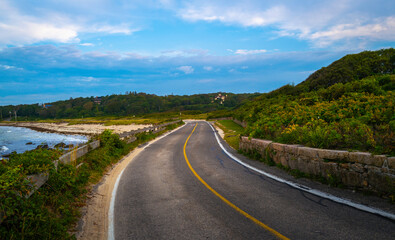 Curved coastal asphalt road around the green hill and dramatic cloudscape in Woods Hole on Cape...