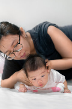 Little two month asian baby lying on stomach and try raised her neck, Asian mother come to help her daughter,  Family concept.;