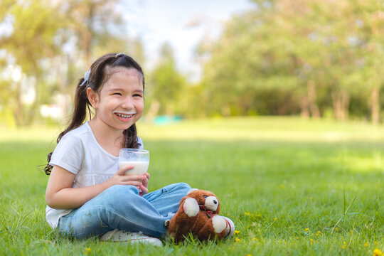Caucasian mix girs drinking milk from glass siting on grass at outdoor park, Whiskers from milk, Good nutrition of children concept.