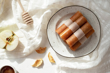 Raw fruit pastille rolls, apple marshmallow with honey on a plate and white tablecloth. Healthy sweets.