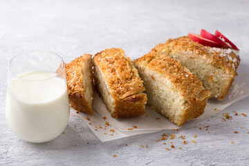 Coconut cake, mannik with apples and cream in a ceramic baking dish on a light gray textured background. Delicious homemade food
