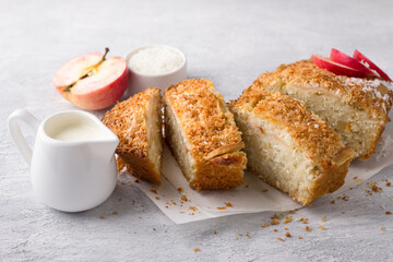 Coconut cake, mannik with apples and cream in a ceramic baking dish on a light gray textured background. Delicious homemade food