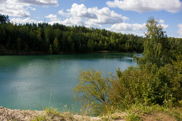 Outskirts of Grodno, Belarus. Early autumn landscape. Green lake surrounded by forest trees, blue sky with white clouds.