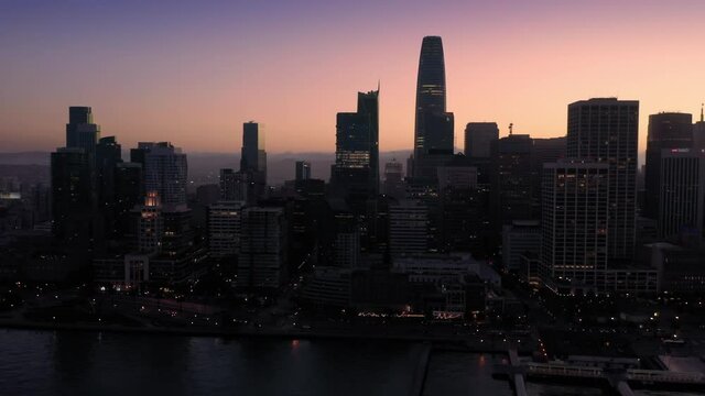 Aerial: Embarcadero and San Francisco city skyline silhouette at sunset, USA