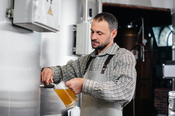 A young bearded brewer conducts quality control of freshly brewed beer in the brewery.