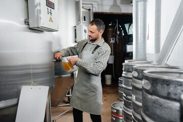 A young bearded brewer conducts quality control of freshly brewed beer in the brewery.