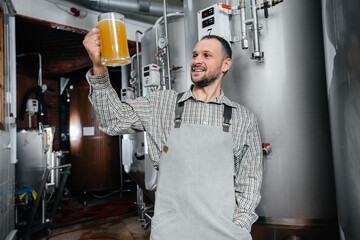A young bearded brewer conducts quality control of freshly brewed beer in the brewery.