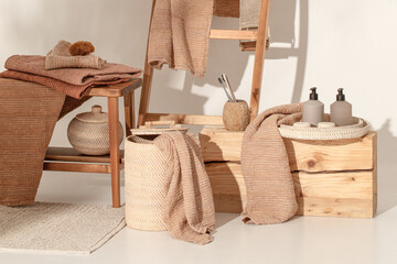 Fototapeta na wymiar Natural waffle linen towels in earth tones on wood bench and towel ladder with bamboo toothbrushes, rattan baskets, and soap dispenser. Daily body care, spa and wellness zero waste bathroom concept