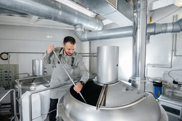 A young male brewer is engaged in the brewing process in a small brewery. Beer production.